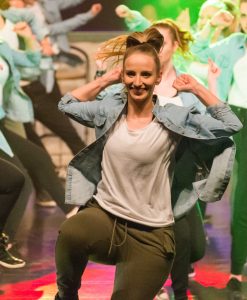 Tine while dancing. Wearing a white shirt, jeans jacket and khaki green joggers.